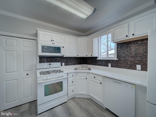 kitchen with a sink, white appliances, white cabinets, crown molding, and decorative backsplash