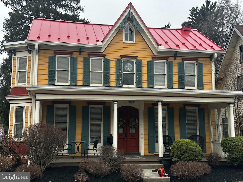 view of front of property featuring metal roof, covered porch, a chimney, and a standing seam roof