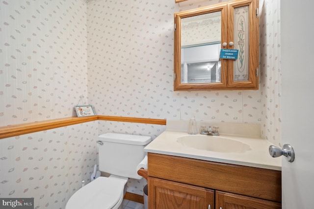 bathroom featuring toilet, vanity, and wallpapered walls