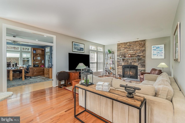 living area with light wood finished floors, a fireplace, and a ceiling fan