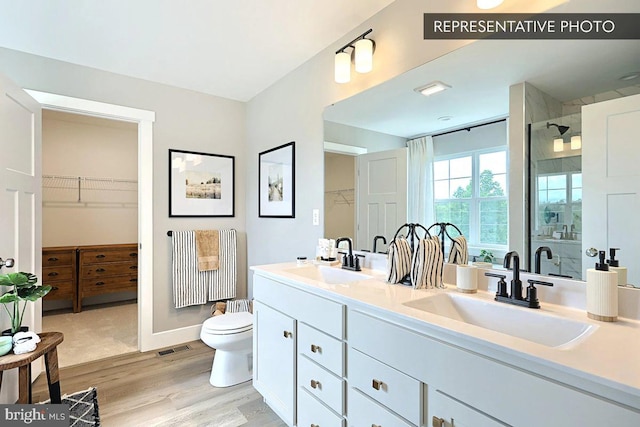 full bath featuring a shower stall, wood finished floors, double vanity, and a sink