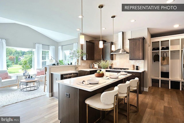 kitchen with dark brown cabinets, dishwasher, wall chimney exhaust hood, and a sink