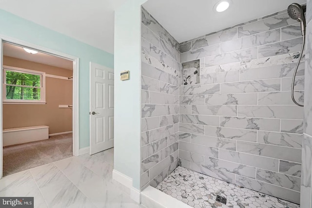 bathroom with marble finish floor, tiled shower, and baseboards