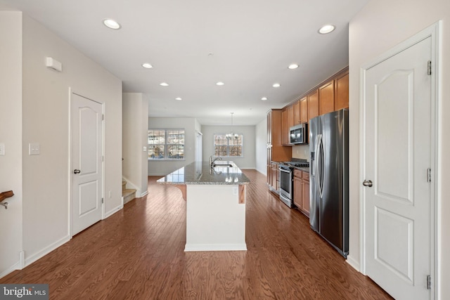 kitchen with an island with sink, a sink, stainless steel appliances, dark wood-type flooring, and a kitchen breakfast bar