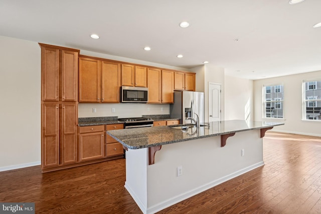 kitchen featuring a kitchen bar, dark wood-type flooring, a center island with sink, a sink, and stainless steel appliances