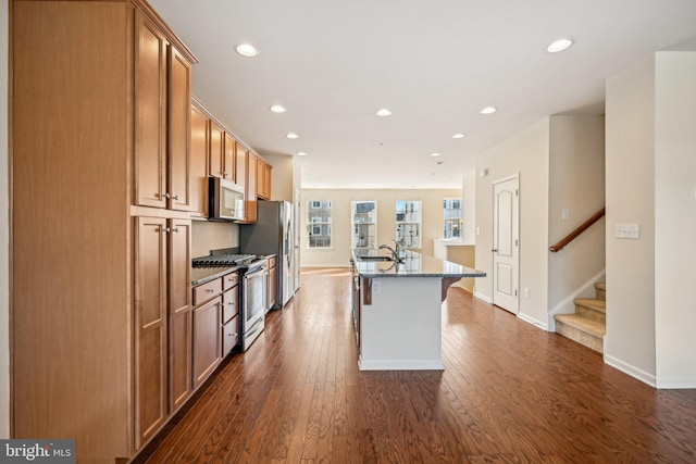 kitchen featuring a center island with sink, dark stone counters, dark wood-style floors, stainless steel appliances, and a sink