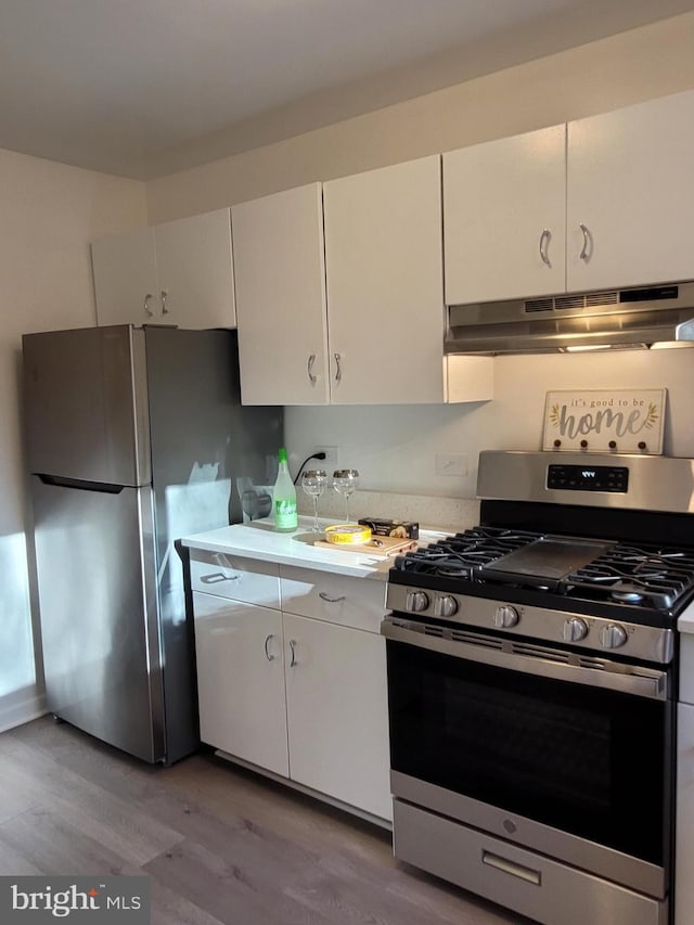 kitchen with light wood finished floors, under cabinet range hood, light countertops, stainless steel appliances, and white cabinetry