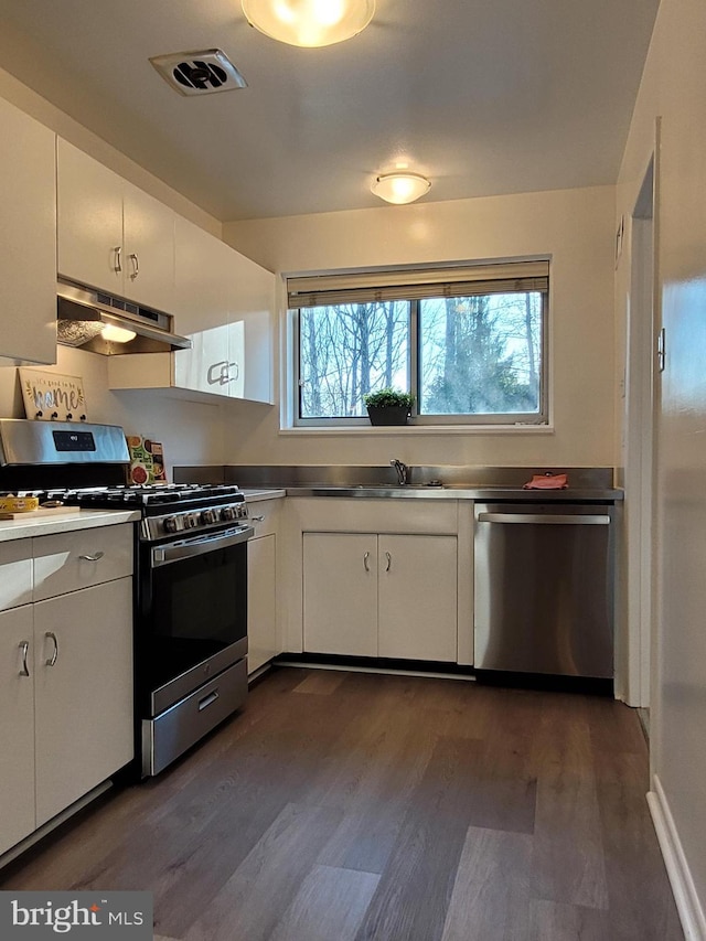 kitchen featuring visible vents, under cabinet range hood, appliances with stainless steel finishes, white cabinetry, and a sink