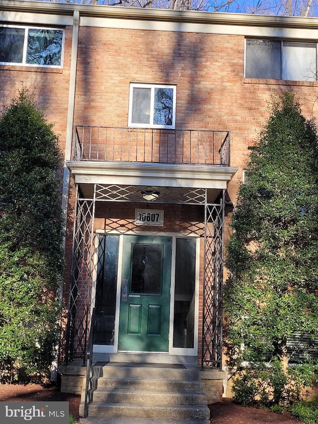 view of exterior entry with a balcony and brick siding