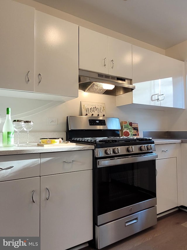 kitchen featuring under cabinet range hood, light countertops, stainless steel gas stove, white cabinets, and dark wood-style flooring