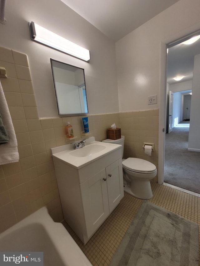 bathroom with a wainscoted wall, toilet, vanity, tile patterned floors, and tile walls