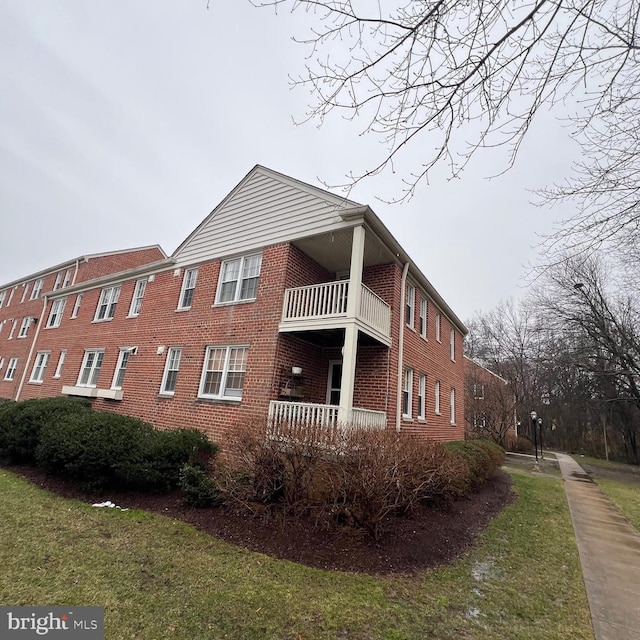 view of side of property with a yard, a balcony, and brick siding