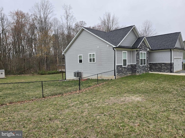 view of side of property with central AC unit, a yard, fence, and stone siding