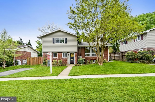 tri-level home with brick siding, a front lawn, and fence