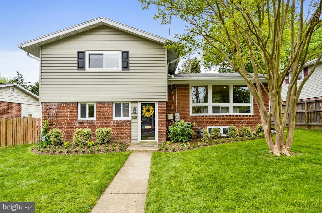 split level home featuring brick siding, a front yard, and fence