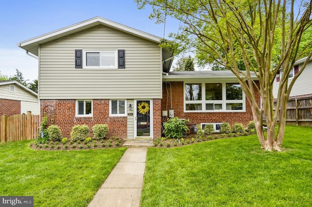 split level home featuring brick siding, a front yard, and fence