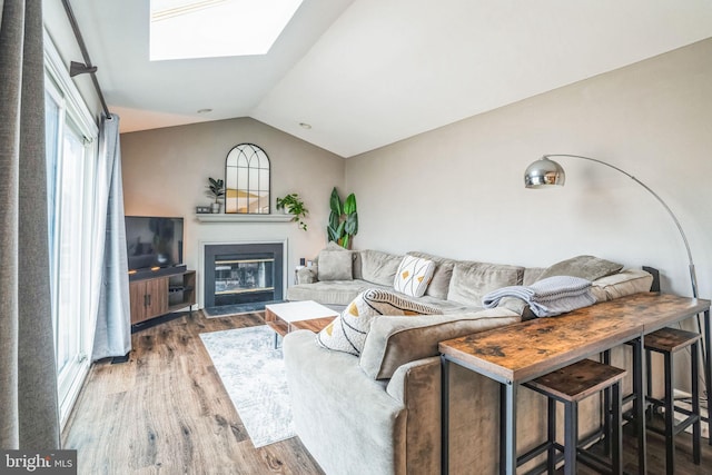 living area featuring a glass covered fireplace, vaulted ceiling with skylight, and wood finished floors