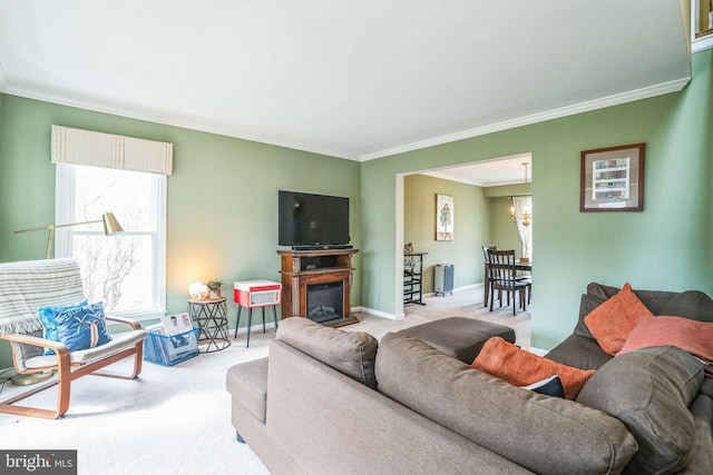 living room with baseboards, a chandelier, ornamental molding, carpet floors, and a glass covered fireplace