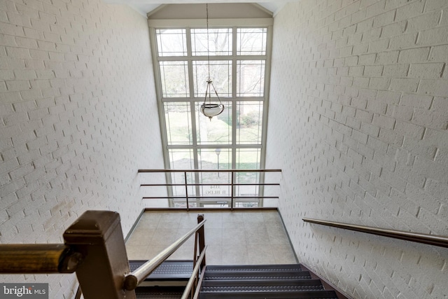 staircase with tile patterned floors, lofted ceiling, and brick wall