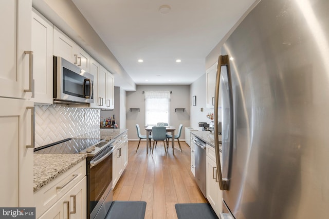 kitchen featuring light stone countertops, white cabinets, light wood-style floors, appliances with stainless steel finishes, and tasteful backsplash