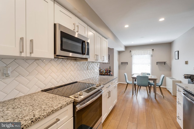 kitchen with light stone counters, stainless steel appliances, white cabinets, tasteful backsplash, and light wood-type flooring