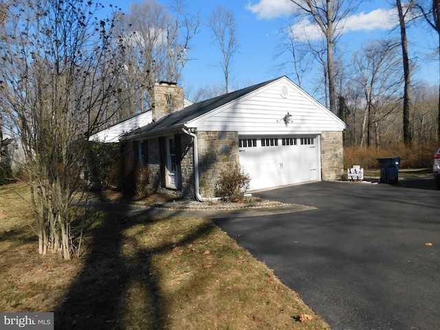 view of side of home with aphalt driveway, stone siding, a chimney, and a garage