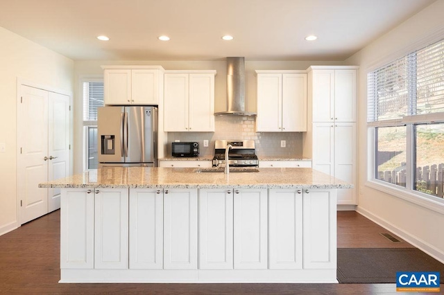 kitchen featuring visible vents, a sink, stainless steel appliances, wall chimney exhaust hood, and a kitchen island with sink