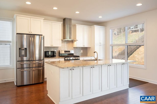 kitchen featuring tasteful backsplash, a sink, appliances with stainless steel finishes, wall chimney exhaust hood, and a kitchen island with sink