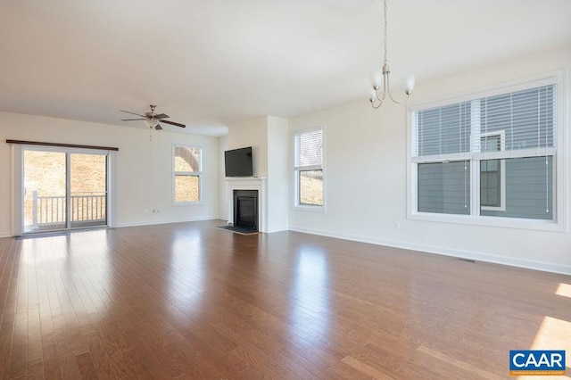 unfurnished living room featuring baseboards, a fireplace with flush hearth, wood finished floors, and ceiling fan with notable chandelier