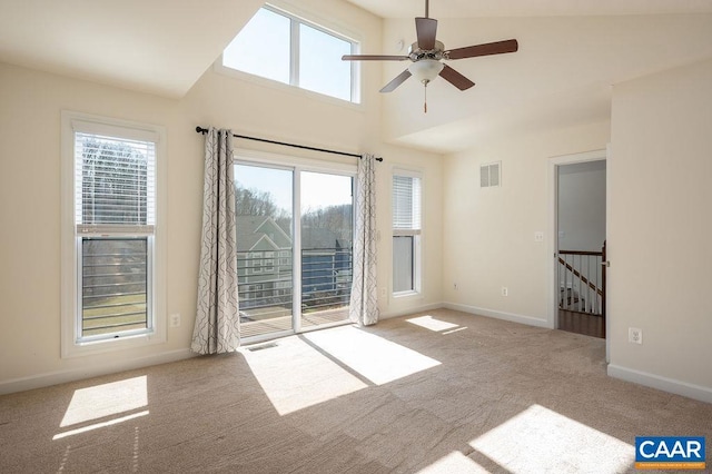 carpeted spare room featuring visible vents, baseboards, ceiling fan, and a towering ceiling