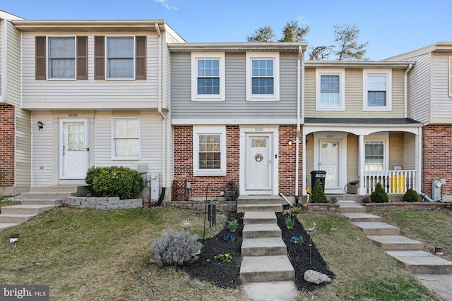 view of property featuring brick siding, covered porch, and a front yard