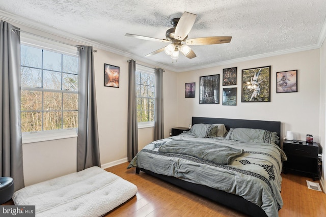 bedroom with ornamental molding, a ceiling fan, a textured ceiling, wood finished floors, and baseboards