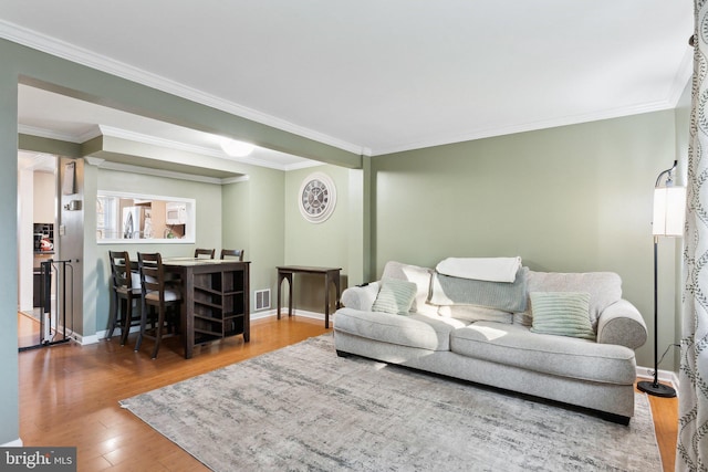 living area with crown molding, wood finished floors, baseboards, and visible vents