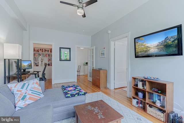 living area with light wood-style flooring, built in shelves, baseboards, and a ceiling fan