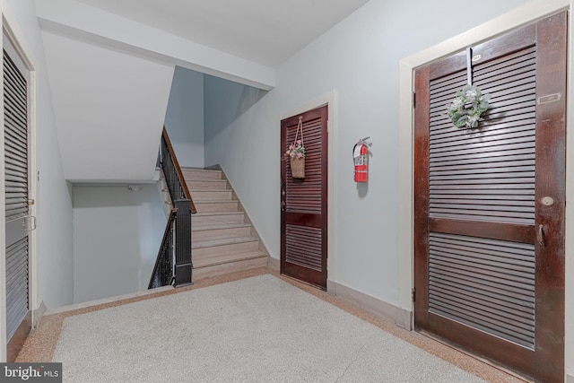 foyer entrance with stairs, speckled floor, and baseboards