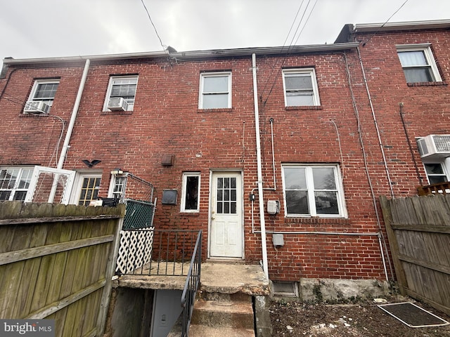 rear view of house with brick siding, cooling unit, a wall mounted AC, and fence