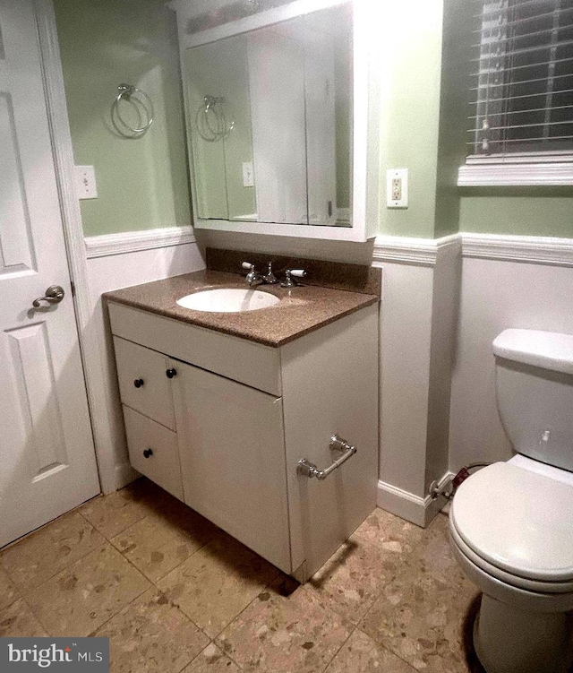 half bath featuring vanity, toilet, and a wainscoted wall