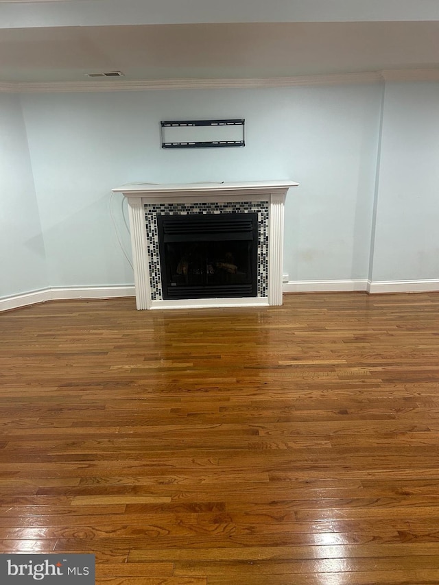 interior details featuring baseboards, wood finished floors, a tile fireplace, and ornamental molding