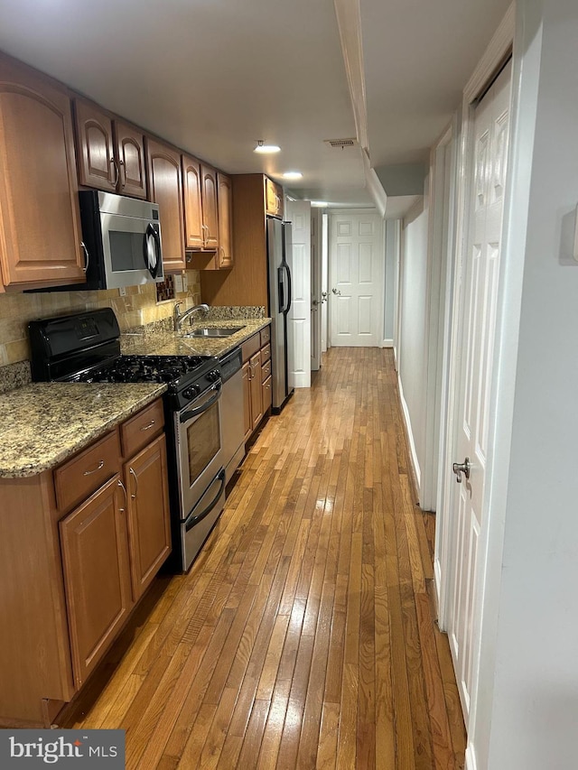 kitchen featuring visible vents, light wood-type flooring, light stone counters, appliances with stainless steel finishes, and a sink