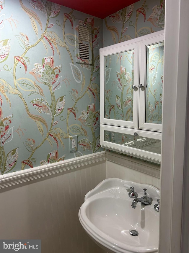 bathroom with wainscoting, wallpapered walls, and a sink