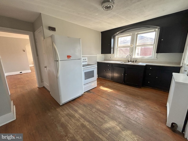 kitchen featuring white appliances, wood finished floors, a sink, light countertops, and dark cabinets