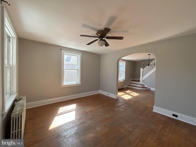 unfurnished room with radiator, dark wood-style floors, arched walkways, and a wealth of natural light