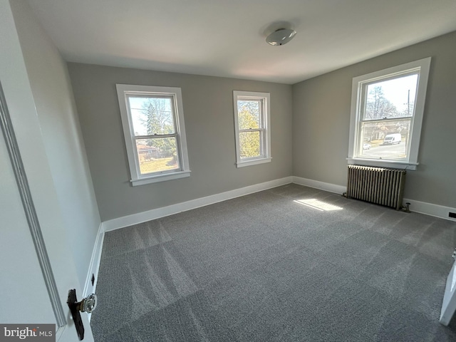 spare room featuring dark carpet, radiator, and baseboards