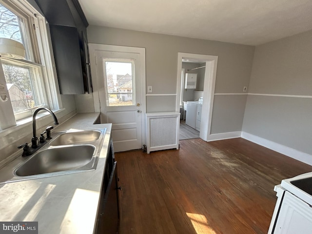 kitchen with washing machine and clothes dryer, radiator, dark wood-type flooring, light countertops, and a sink