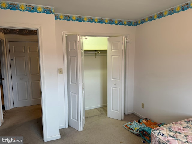 bedroom with a closet, light colored carpet, and baseboards