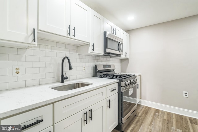 kitchen featuring a sink, stainless steel appliances, white cabinets, light wood finished floors, and baseboards