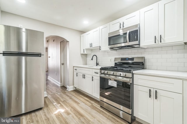 kitchen featuring arched walkways, light wood-style flooring, appliances with stainless steel finishes, and white cabinets