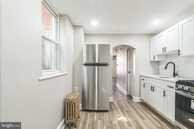 kitchen with a sink, stainless steel appliances, arched walkways, radiator, and decorative backsplash