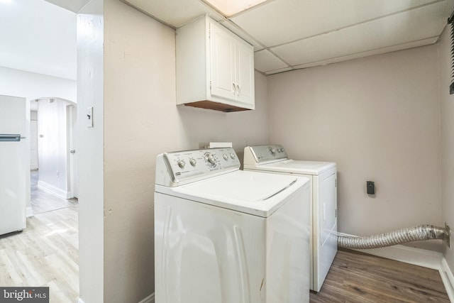 clothes washing area featuring arched walkways, cabinet space, light wood-style flooring, and baseboards