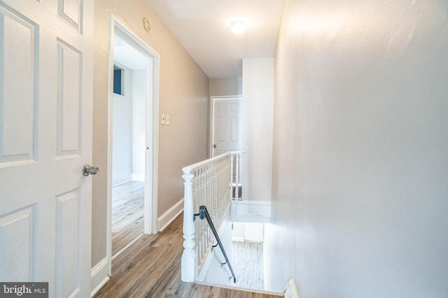 hall featuring an upstairs landing, baseboards, and wood finished floors